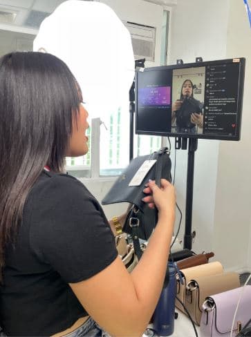 Host shows a black handbag to viewers beside the livestream monitor